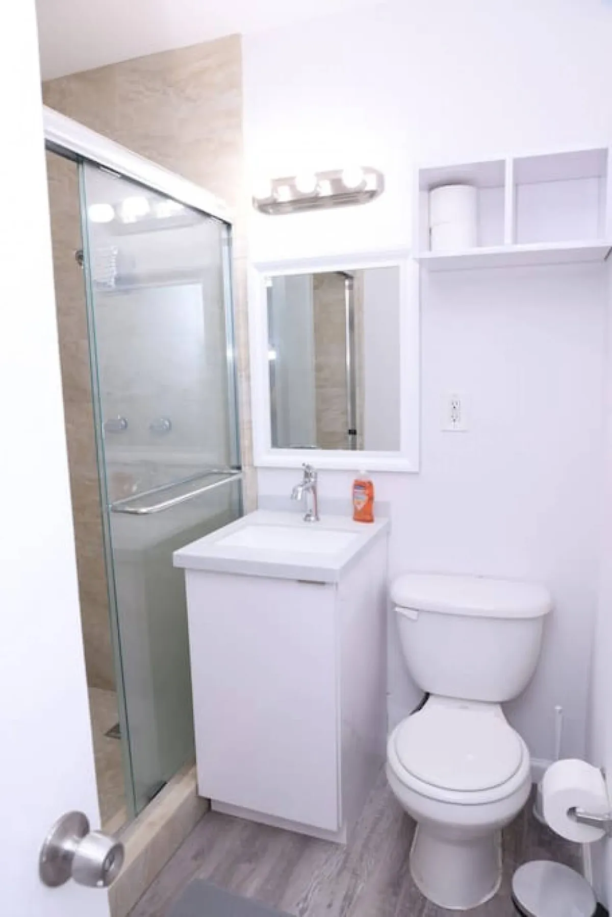 A bright, modern bathroom featuring a sleek white vanity with a chrome faucet, a glass-enclosed shower, and a toilet. The space is organized and clean, with a large mirror and soft lighting creating a fresh and inviting atmosphere.